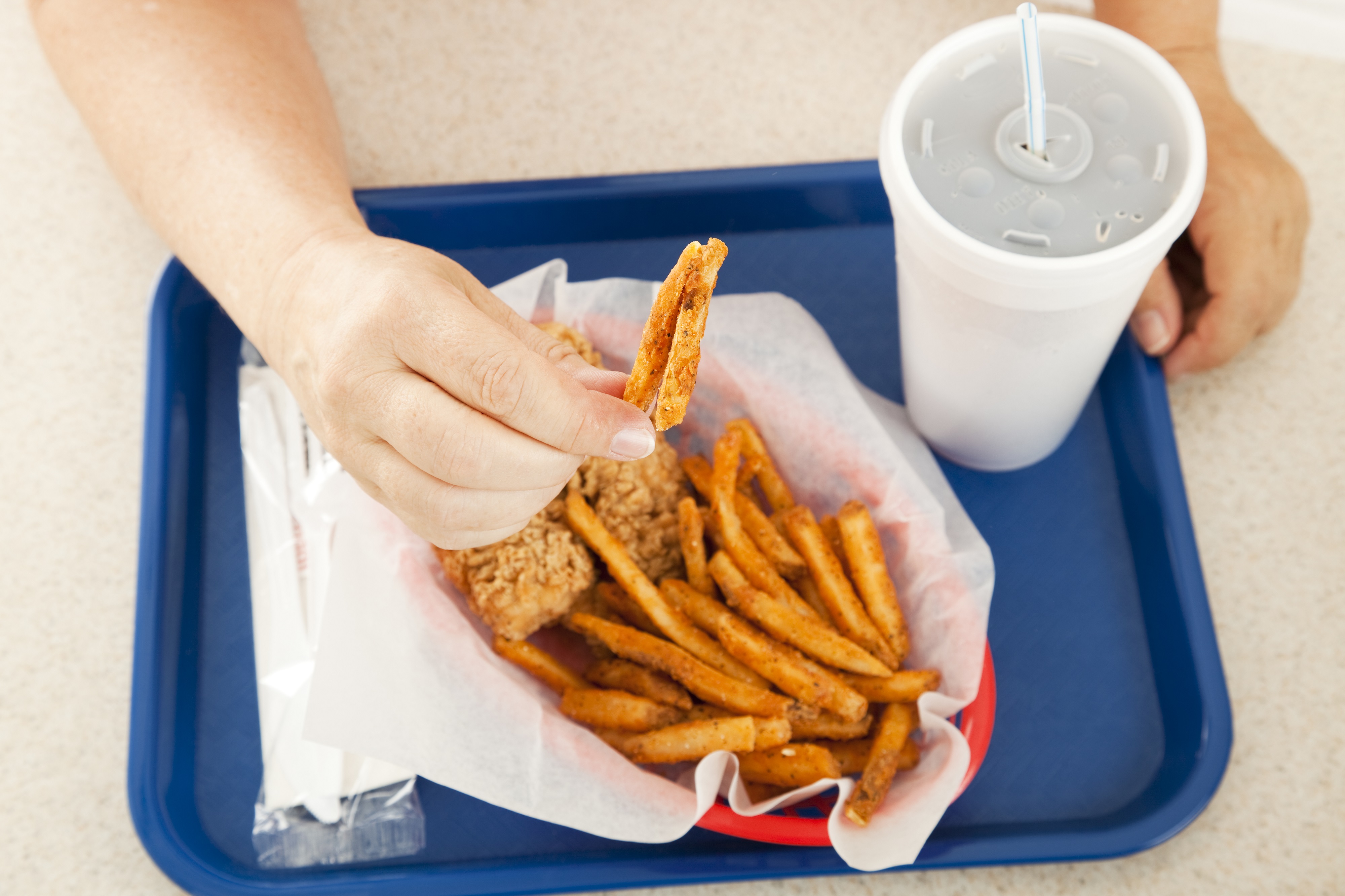 A plate of greasy fast food, with the customer holding up a greasy french fried potato to the camera.  Focus on the hand and the fry.