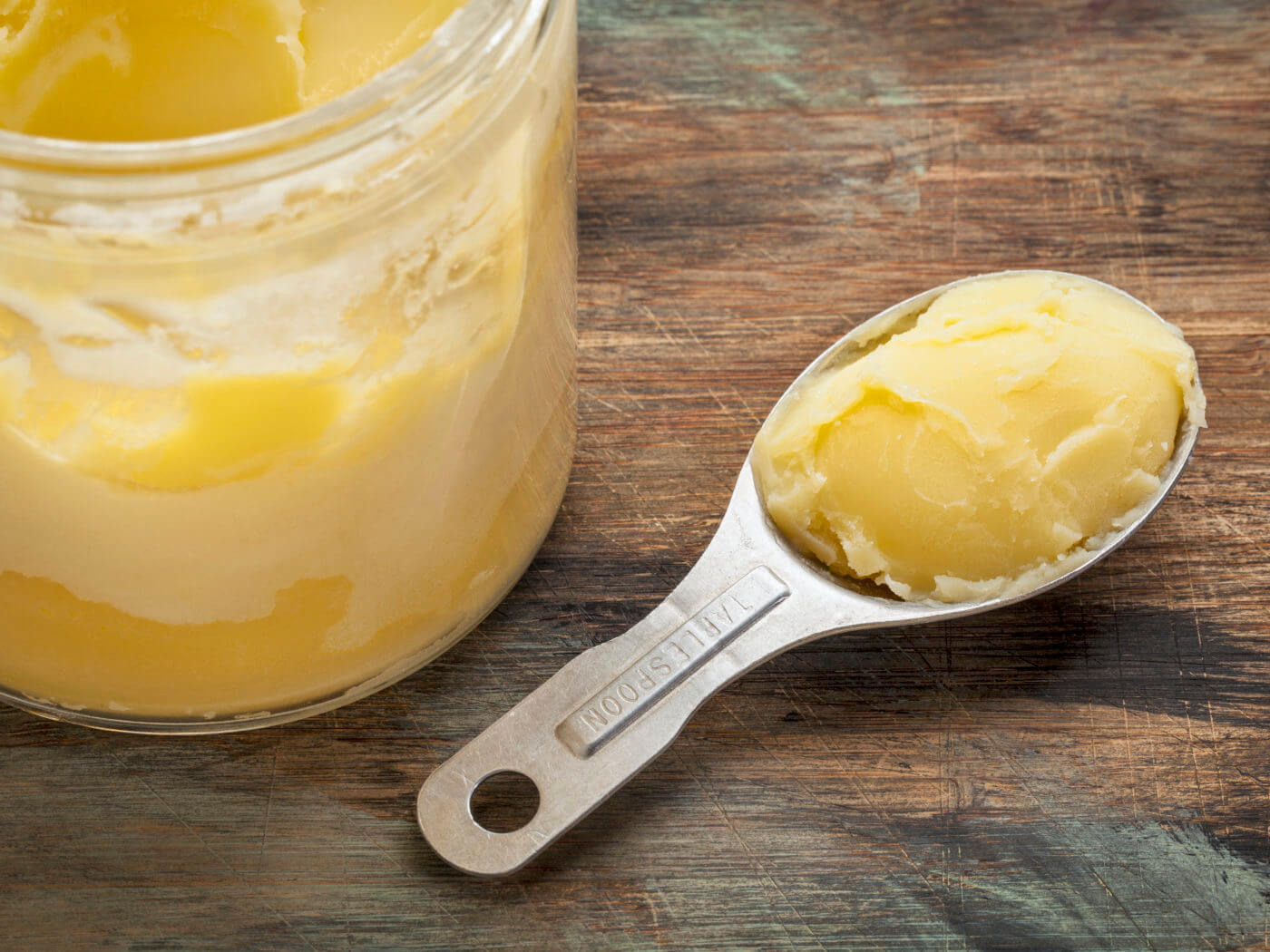 jar and measuring tablespoon of ghee - clarified butter on grunge wood
