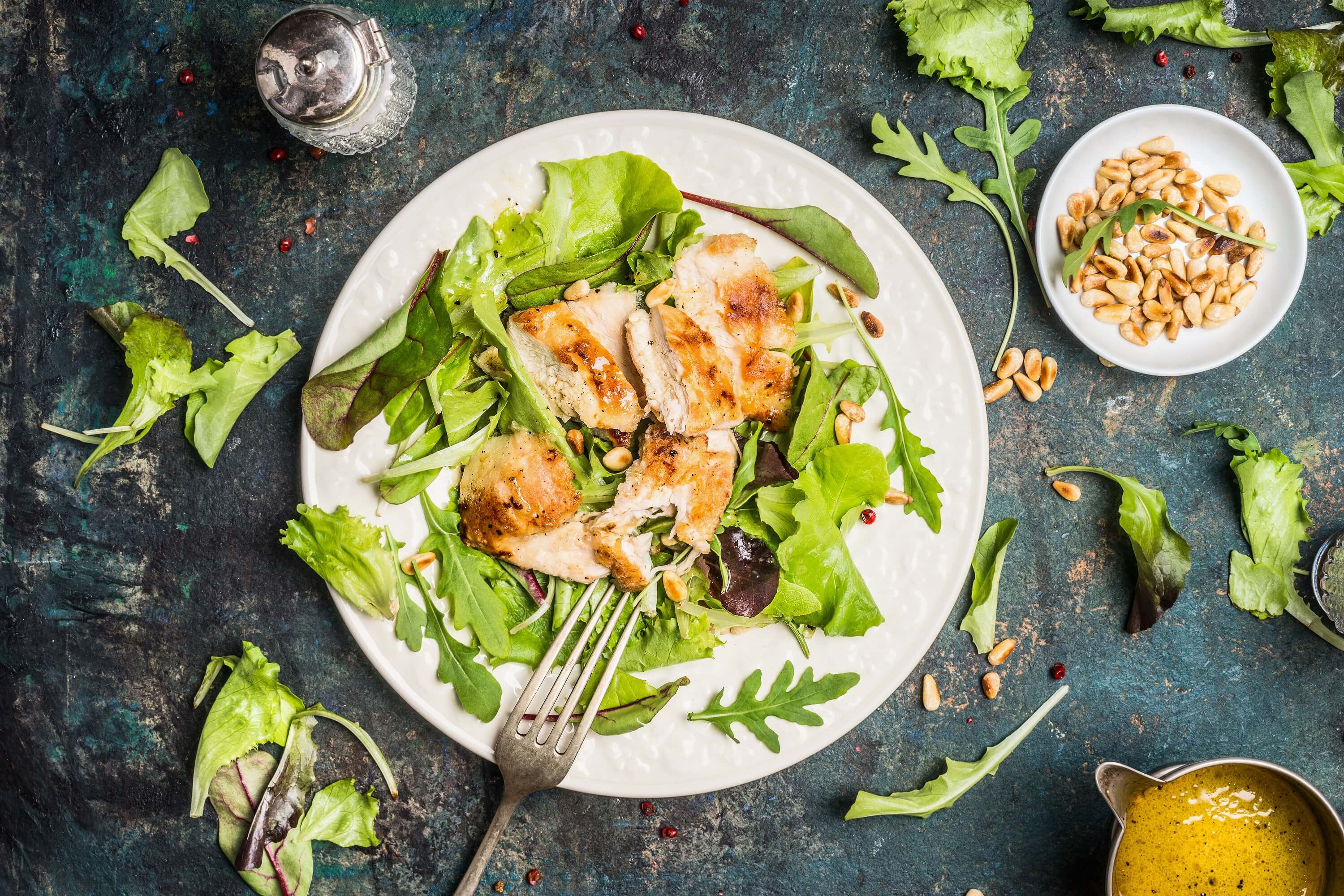 Chicken green salad served on rustic table with pine nuts and oil dressing, top view