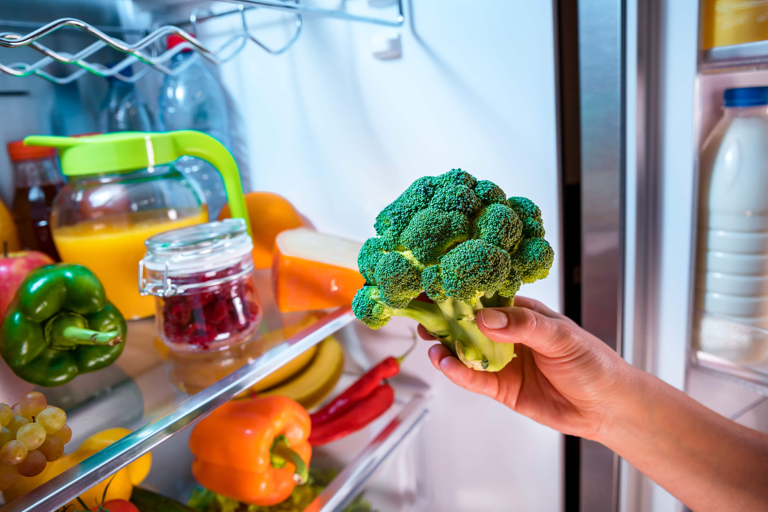 Woman takes the broccoli from the open refrigerator. Healthy food.
