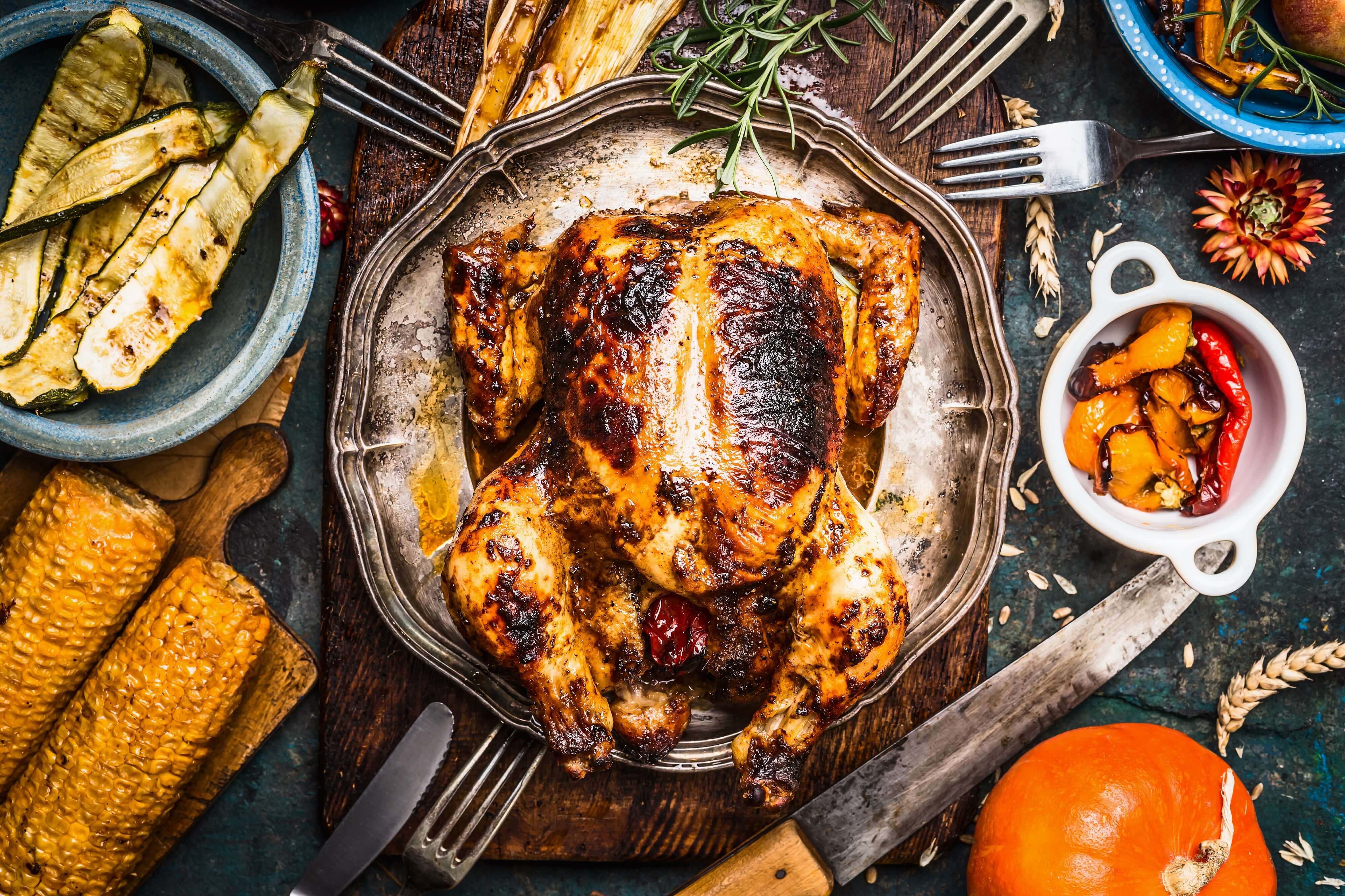 Roasted  whole turkey or chicken with organic harvest vegetables and pumpkin for Thanksgiving dinner on rustic table background, top view