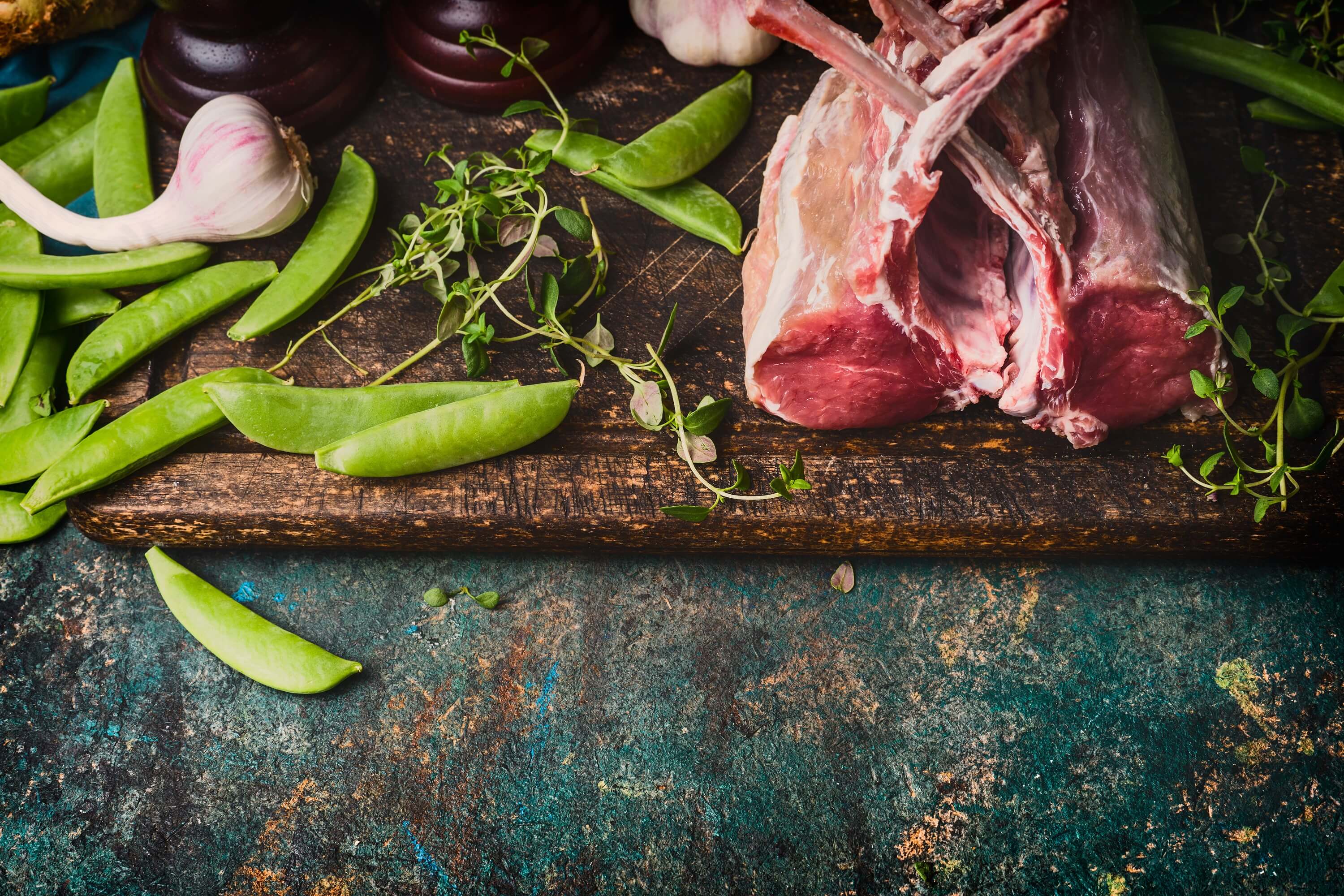 Rack of lamb with green pea pods, cooking preparation on rustic background, top view, border