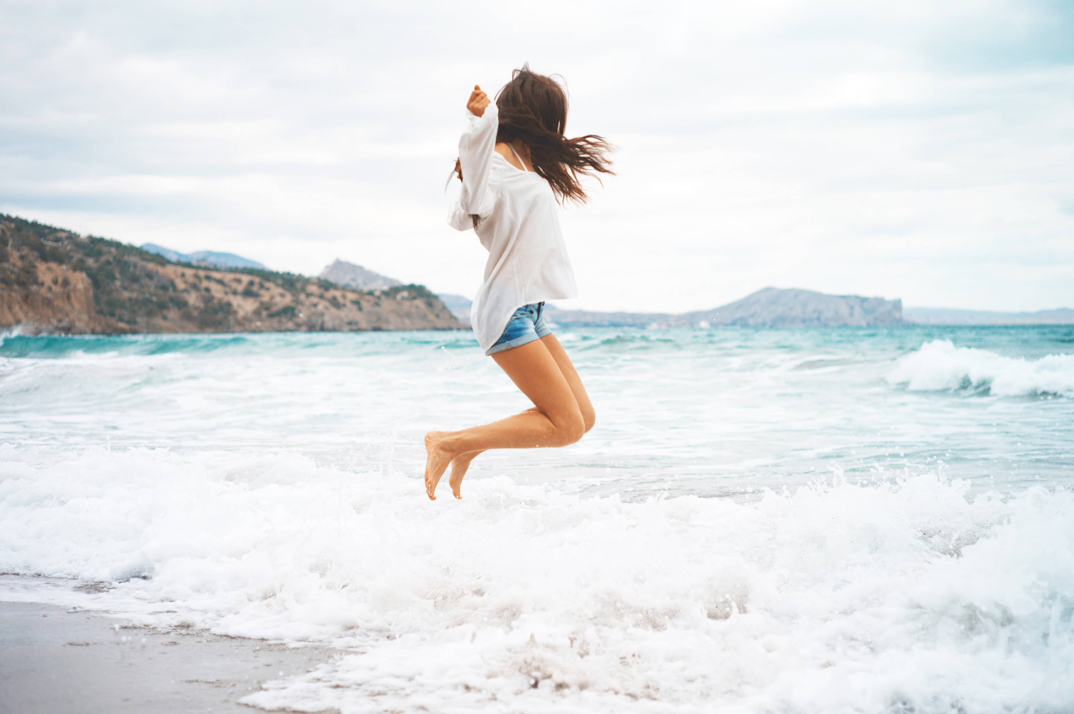 Outdoor photo of beautiful young woman jumping at the sea